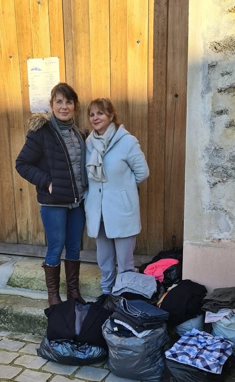 La photo montre Catherine et Isabelle devant l'église Sainte-Christine avec les sacs de vêtements collectés pour l'association "Solidarité Partage 77"