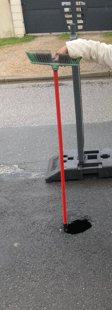 Photo illustrant le fait qu'un balai d'un mètre 20 peut être enfoncé dans le trou apparu dans la chaussée de la D21 le 12 mai 2024